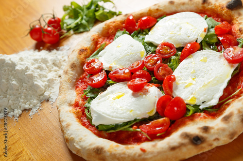 Typical Italian Pizza, ingredients in background on wood table