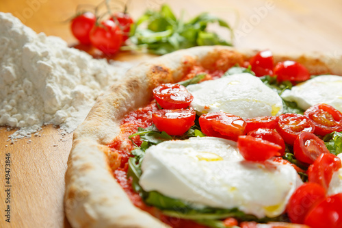 Italian Pizza with ingredients in background on a wood table