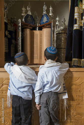 two boys standing in front of holy jewish scripts in a synagogue
