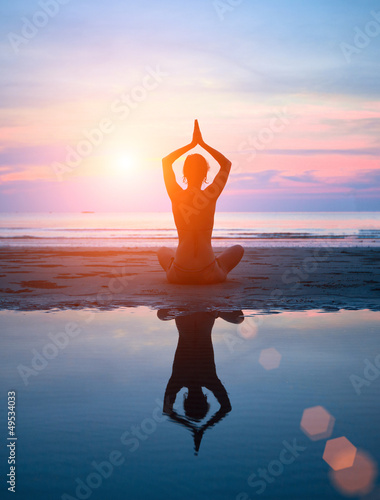 Silhouette of a woman yoga on sea sunset with reflection.