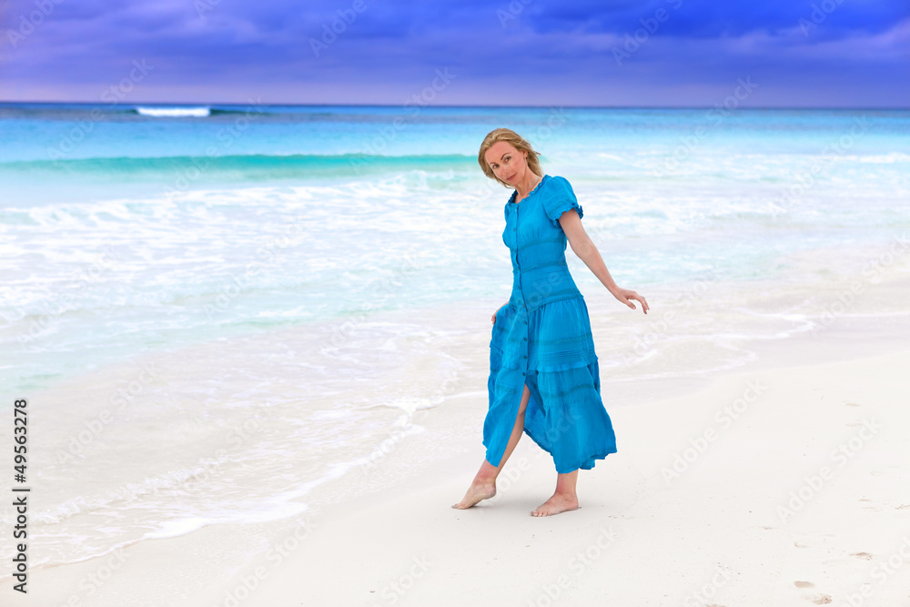 The woman in a long blue dress on the  stormy sea coast