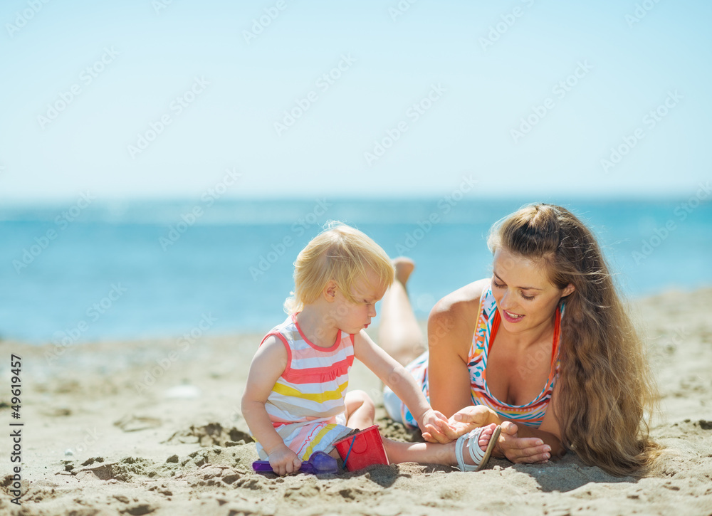 Mother and baby girl playing with sand on beach Mother and baby girl playing with sand on beach