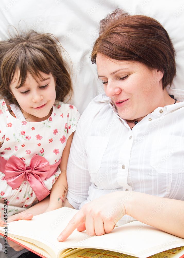 A mother and her little daughter reading a book before sleeping A mother and her little daughter reading a book before sleeping