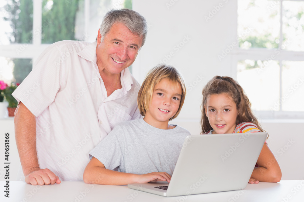 Grandfather and children looking at the camera with laptop in fr Grandfather and children looking at the camera with laptop in fr