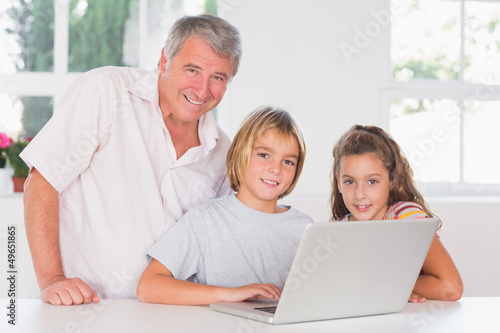 Grandfather and children looking at the camera with laptop in fr