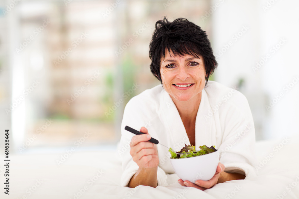 beautiful mature woman lying on bed and eating green salad beautiful mature woman lying on bed and eating green salad