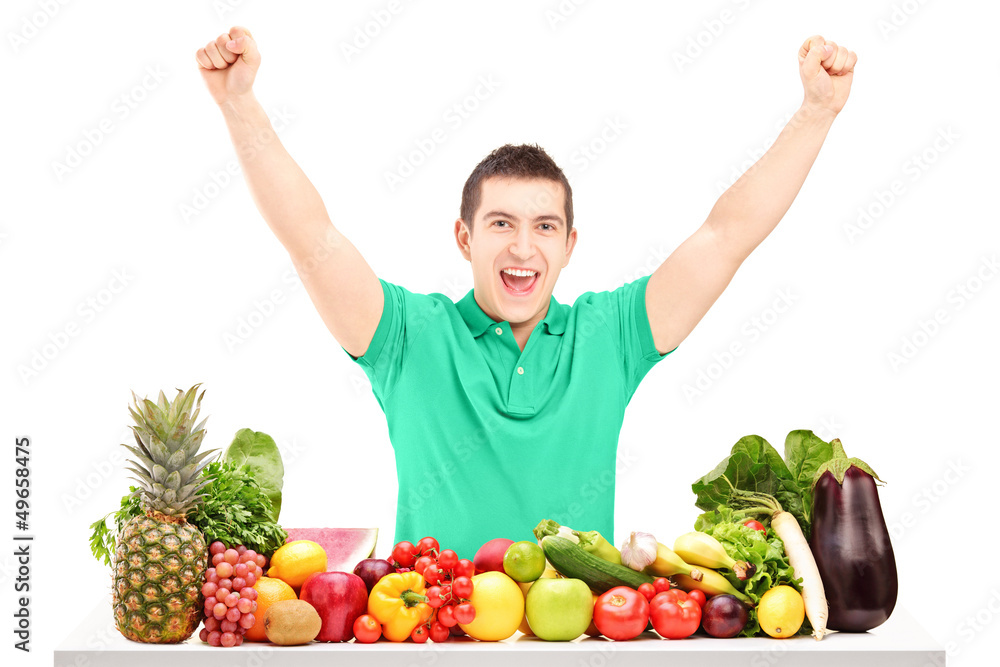 Excited man raising hands and posing with a pile of fruit and ve Excited man raising hands and posing with a pile of fruit and ve