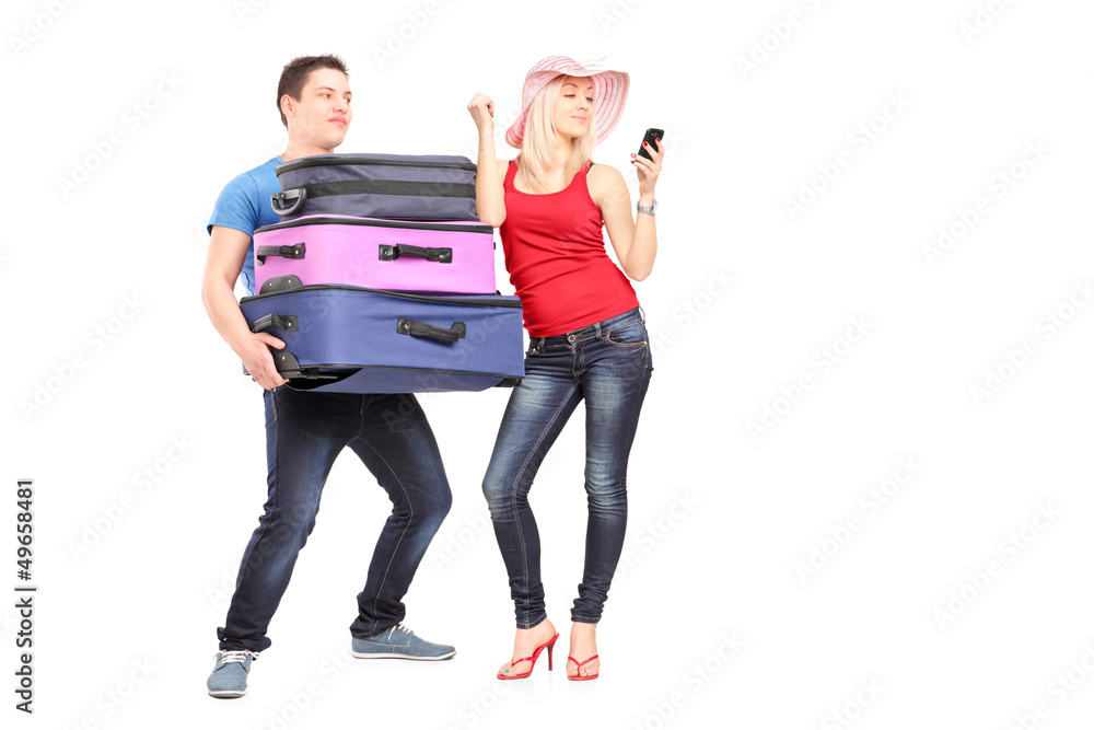 Frustrated man carrying his girlfriend's baggage while she is ma