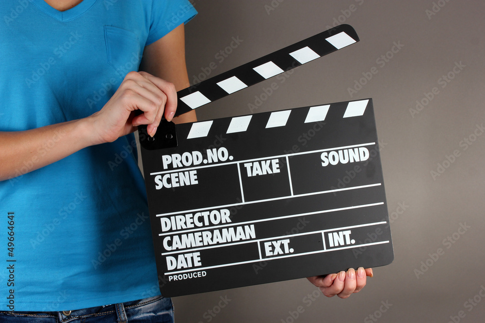 Movie production clapper board in hands on grey background