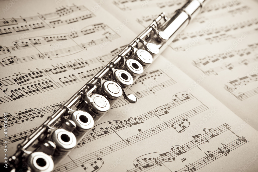 Fototapeta premium Silver flute on an ancient music score background