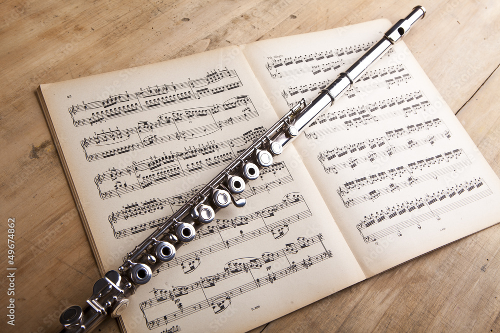 Fototapeta premium Silver flute on an ancient music score background