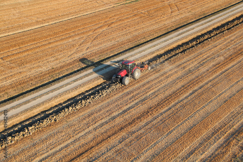 Canvas-taulu Red tractor on field plowing the land at sunset