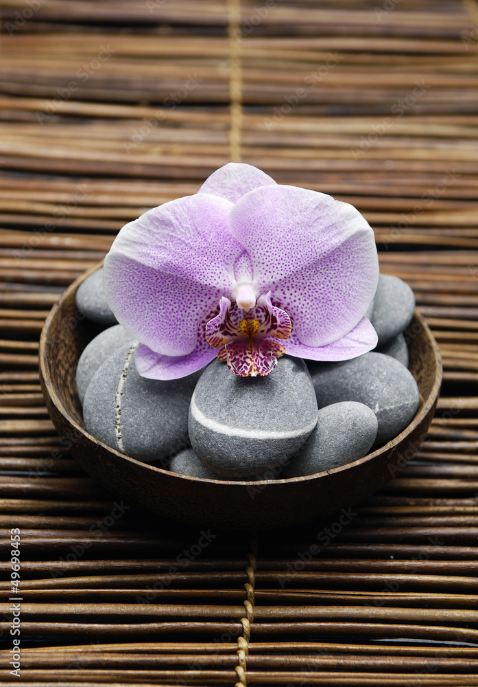 Single orchid with \gray stones in bowl on bamboo mat Single orchid with \gray stones in bowl on bamboo mat