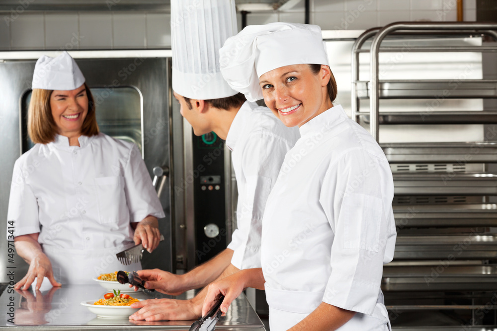 Female Chef With Colleagues In Commercial Kitchen