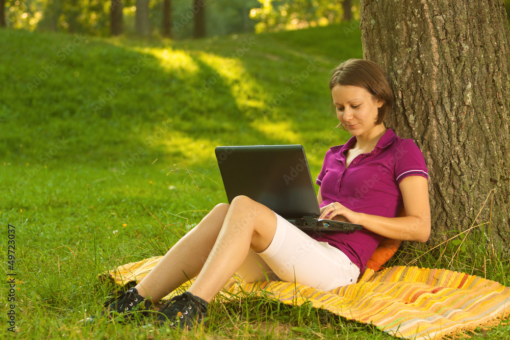 Beautiful young brunette working on a laptop in the park Beautiful young brunette working on a laptop in the park