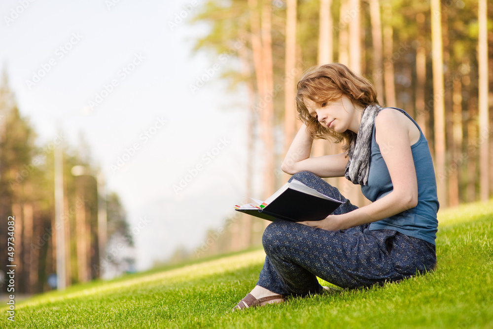 Young woman sitting on green grass and reads book Young woman sitting on green grass and reads book