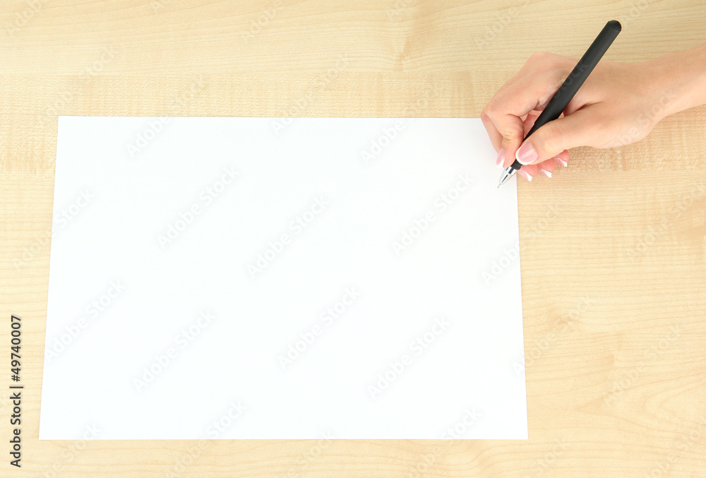 Hand with pen on white paper, on wooden background Hand with pen on white paper, on wooden background