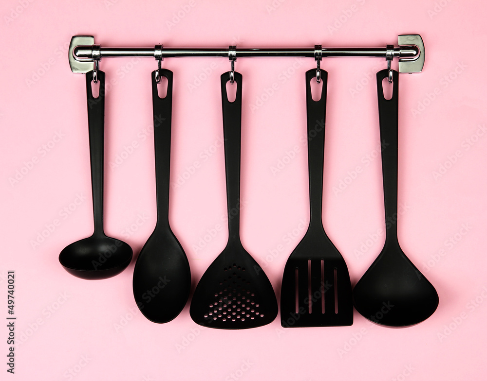 Black kitchen utensils on silver hooks, on pink background Black kitchen utensils on silver hooks, on pink background