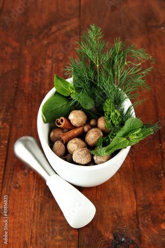 Herbs and spices in ceramic mortar, on wooden background