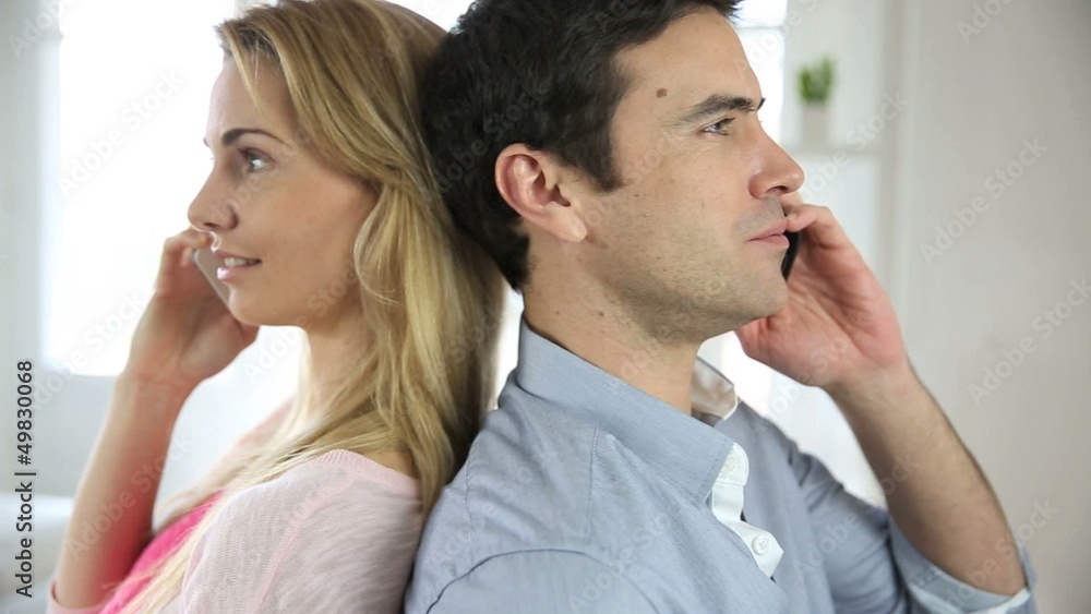 Couple using smartphone, sitting back to back Couple using smartphone, sitting back to back