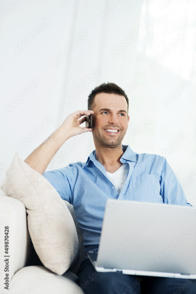 Cheerful man using laptop and talking on mobile phone