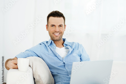 Cheerful man relaxing with laptop and cup of coffee