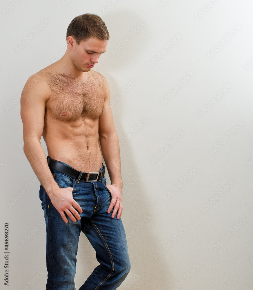 Young handsome guy in jeans with bare torso against the wall