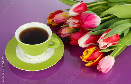 Beautiful tulips in bucket with cup of tea on purple background