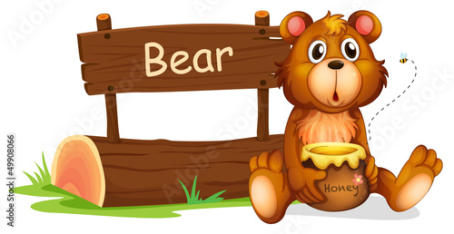 A bear holding a honey beside a wooden signboard
