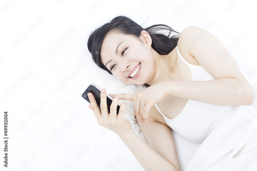 Naklejka premium ベッドでスマートフォンを使う女性