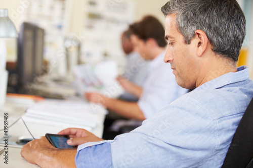 Man Using Mobile Phone At Desk In Busy Creative Office