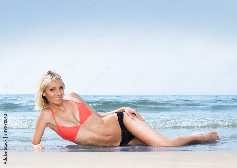 A young and lovely woman in a swimsuit laying on the beach