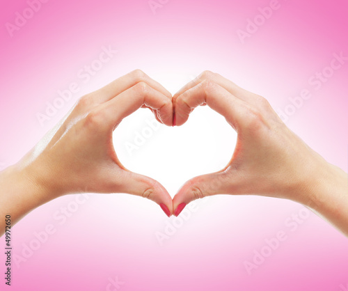 Beautiful female hands in a shape of a heart on pink