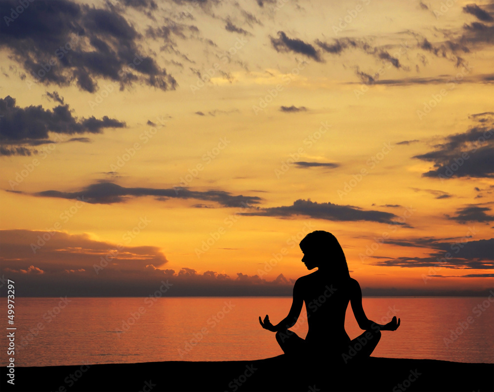 A silhouette of a young woman meditating on a sunset background