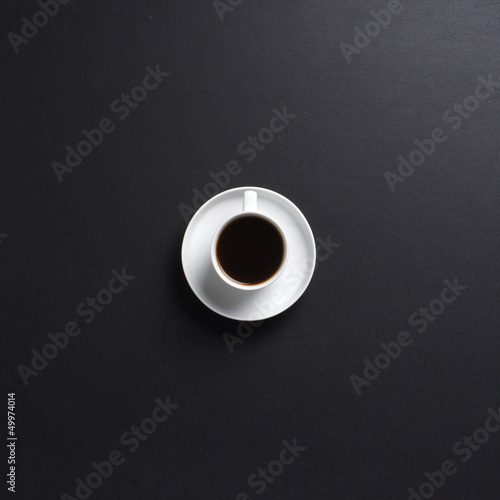 A tiny white cup of coffee on a black table background