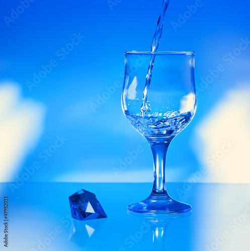 Water pouring into glass on blue background