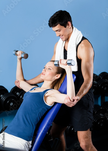Trainer helps woman to exercise with dumbbells in gym