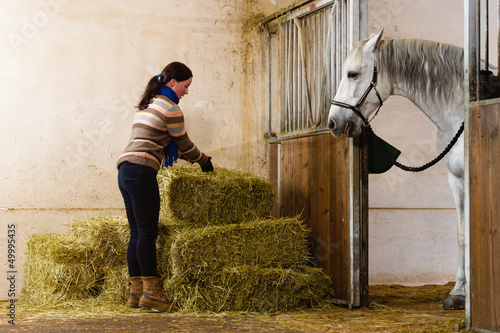 Woman and haystacks, white horse watching alongside