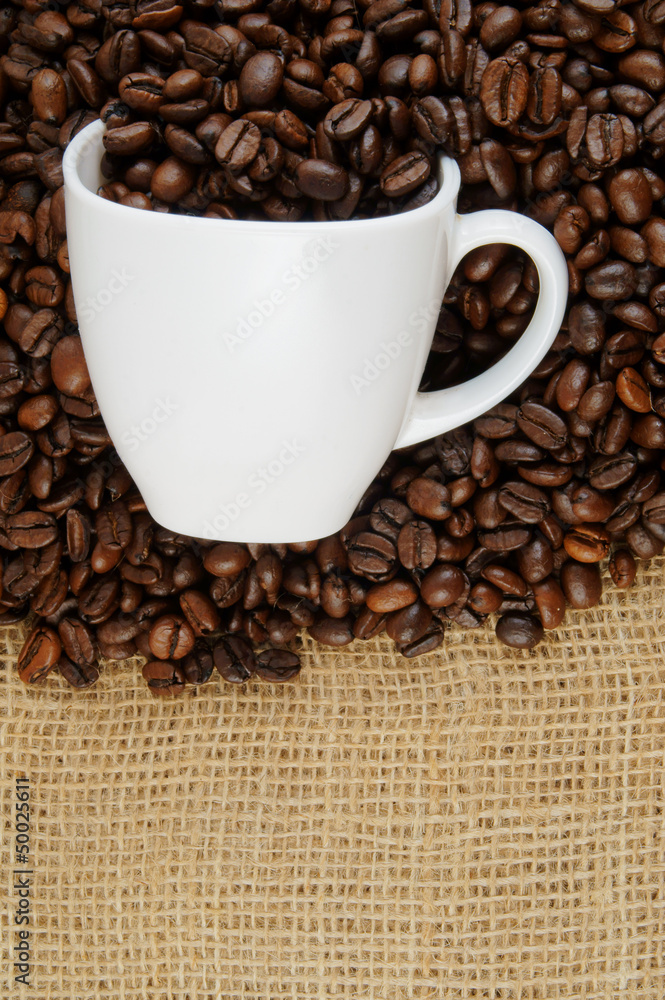 Roasted coffee beans and cup on jute hessian background Roasted coffee beans and cup on jute hessian background