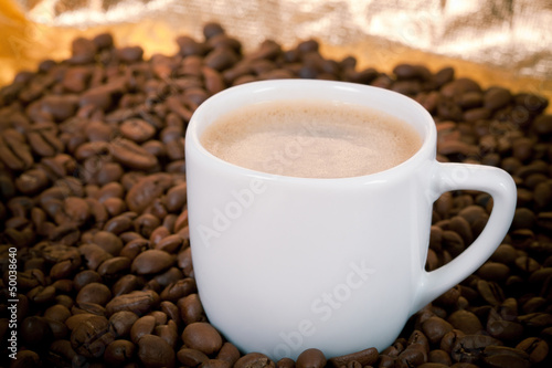 A cup of coffee is on the background of roasted coffee beans