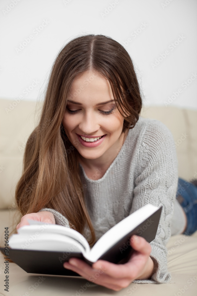 Happy young woman reading book on sofa Happy young woman reading book on sofa