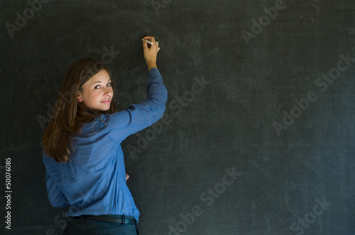 Confident woman teacher writing on blackboard