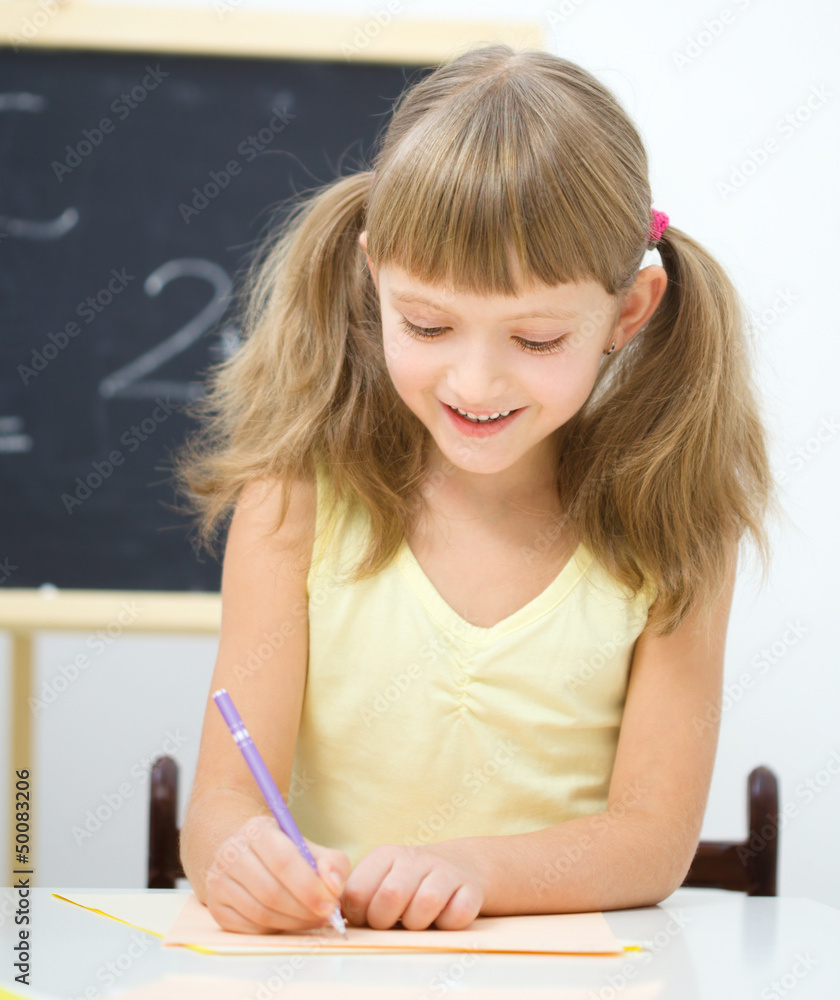 Little girl is writing using a pen