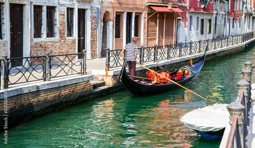 Gondolier paddling his gondola through a small channel in Venice
