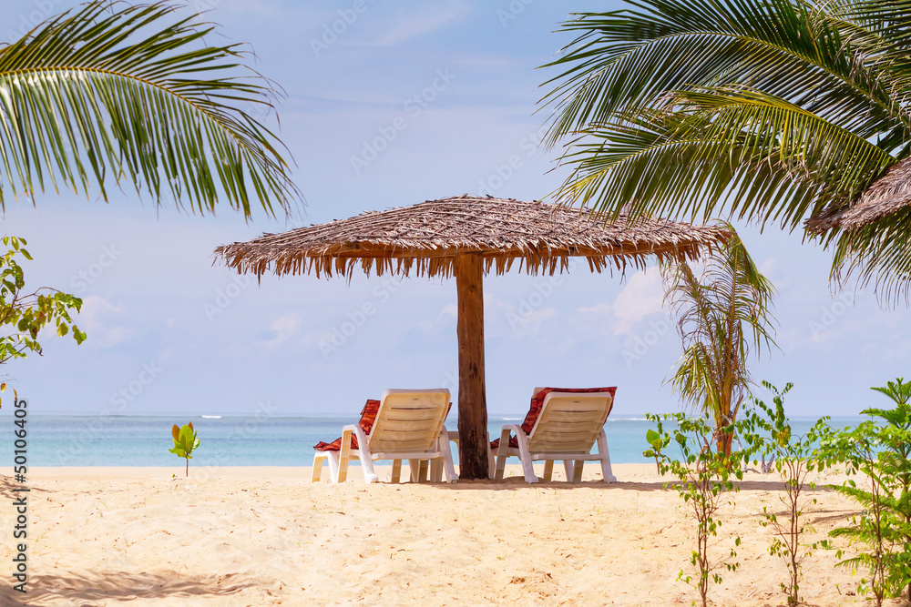 Tropical beach scenery with parasol and deck chairs in Thailand