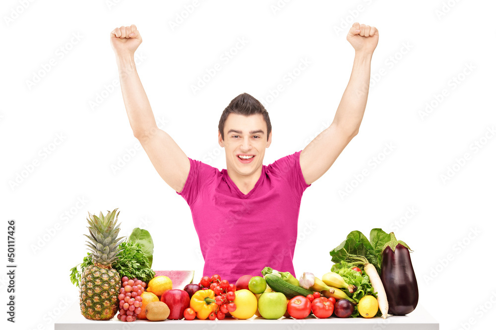 Happy young man raising hands and sitting behind a pile of fruit Happy young man raising hands and sitting behind a pile of fruit
