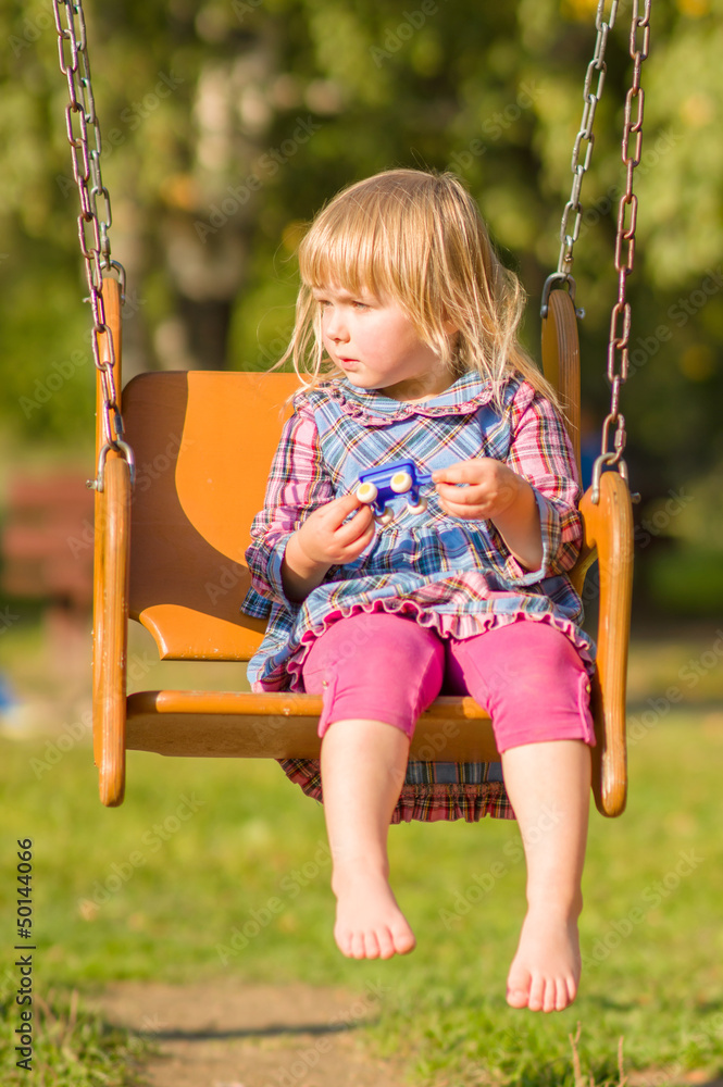 Adorable girl in dress swing on playground in park Adorable girl in dress swing on playground in park