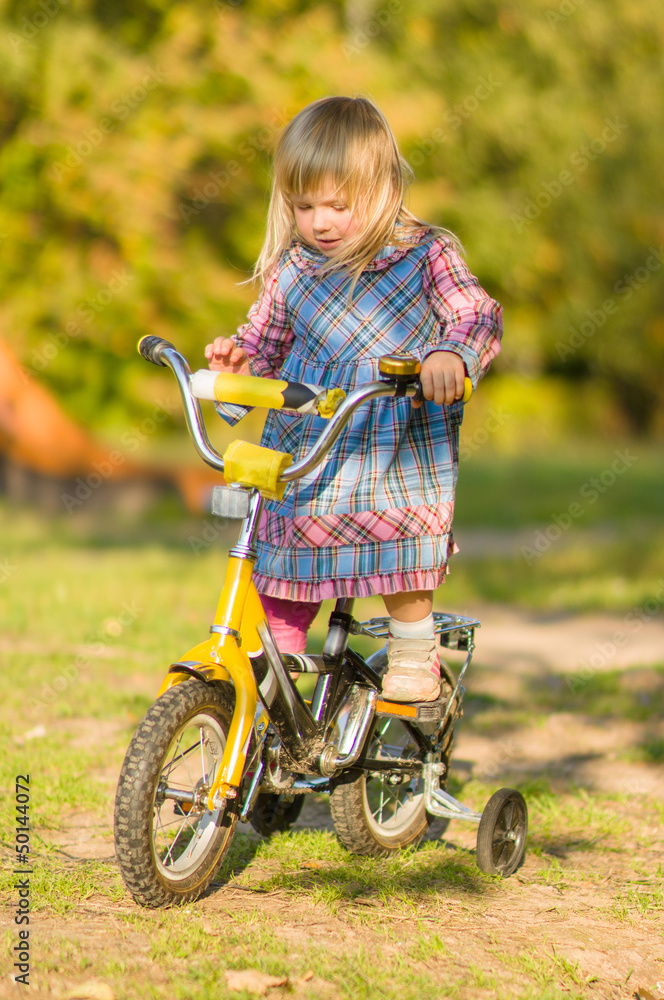 Adorable girl ride on bike with training wheels on playground in Adorable girl ride on bike with training wheels on playground in