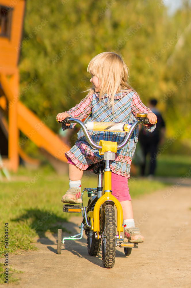 Adorable girl ride on bike with training wheels on playground in Adorable girl ride on bike with training wheels on playground in