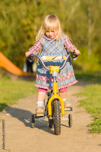 Adorable girl ride on bike with training wheels on playground in